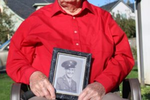 Ken Shold sits outside his home in Washougal on Friday, Nov. 1. He's holding a photo of himself that was taken in the 1940s when Shold was serving in the United States Army during World War II. (Doug Flanagan/Post-Record)