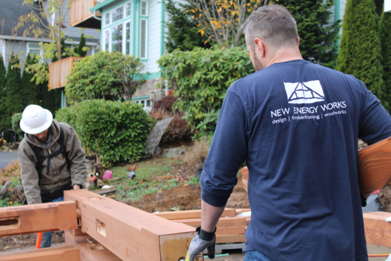 Justin Jaycox, of New Energy Works (right), carries a piece of the timber-framed solar canopy that will support bi-facial solar panels and provide energy to Camas couple Randy Friedman and Debbie Nagano's home and power their electric vehicle.