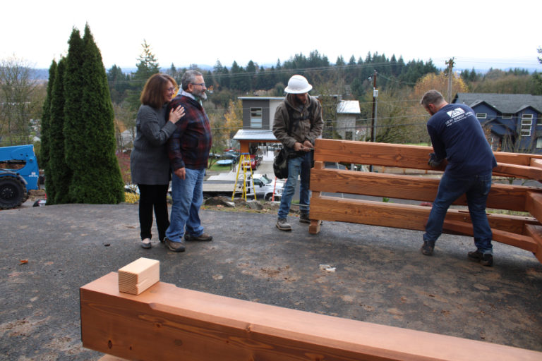 Debbie Nagano (left) and Randy Friedman (second from left), watch as workers from New Energy Works build the timber-frame structure that will support their Camas home's front-yard "solar canopy," which will provide power for their electric vehicle.