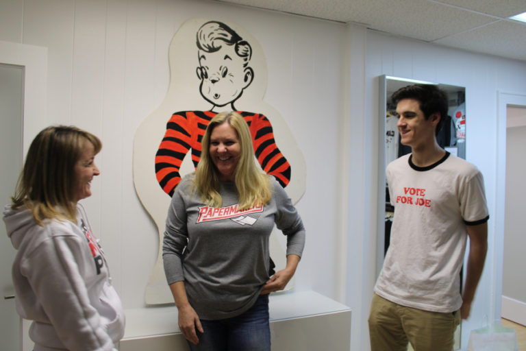 Sherly Obegi (left) and Karen Gibson (center), co-owners of Papermaker Pride, laugh with their intern, Camas High senior Tommy Kelly (right) in front of the &quot;Joe Papermaker&quot; sign they have displayed in their new downtown Camas business.