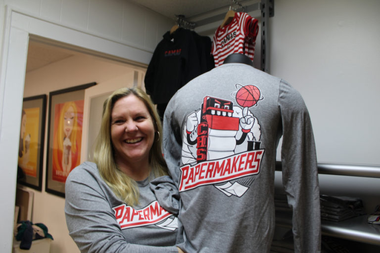 Karen Gibson, a co-owner of Papermaker Pride, shows some of her favorite designs available at the downtown Camas shop: the Camas basketball shirts featuring the Camas Papermakers&#039; &quot;Mean Machine.&quot;