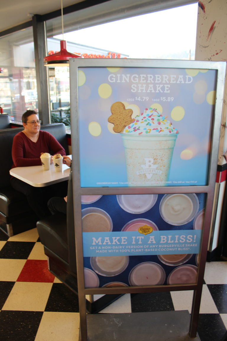 A sign advertising Burgerville’s seasonal Gingerbread Shake sits near the entrance of the Camas Burgerville, while Karen Wood, of Camas, co-owner of McTavish Shortbread, the company that supplied the gingerbread cookies for the seasonal shake, talks to her husband and business partner, Peter Wood (not pictured) on Thursday, Dec.