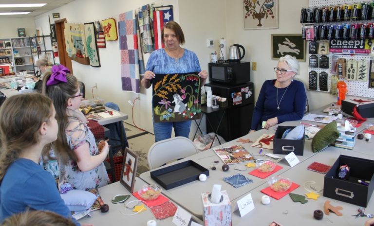 Camas resident Kathy Begier shows off her latest wool applique project to Anna Davis (right) and members of the &quot;applique club&quot; at A Place to Create in Washougal.