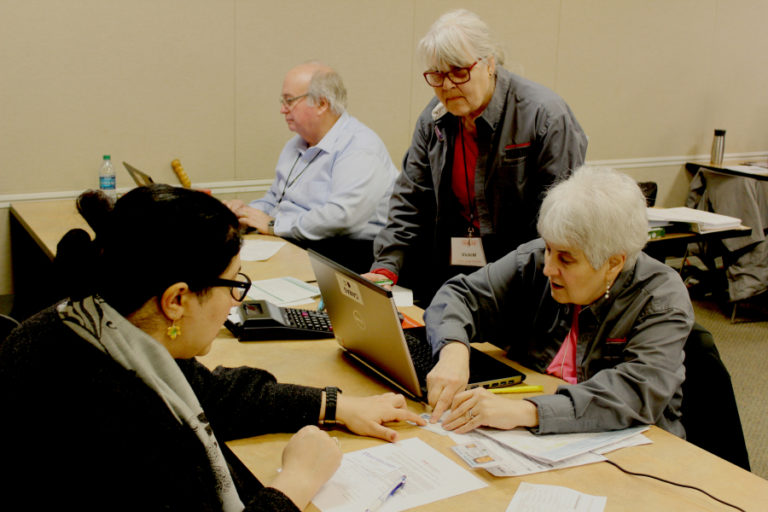 Local AARP Foundation Tax-Aide coordinator Sherry Davis (right) inspects documents provided by taxpayer Nadia Samiee (left) of Vancouver at the Camas Public Library in February 2019, while Tax-Aide counselor Vicki Millard (second from right), of Washougal, watches and Tax-Aide counselor Mike Leonardich (third from right), of Vancouver, works on another tax return.