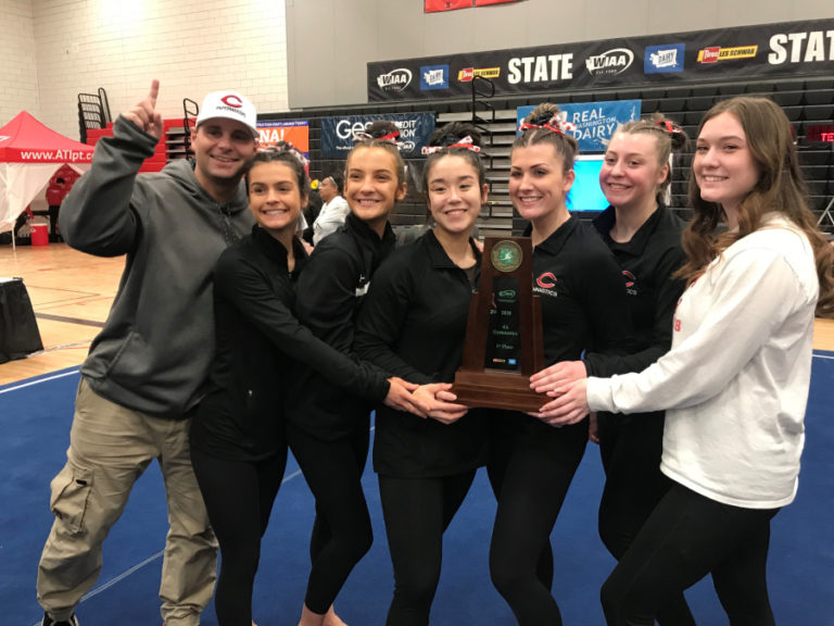 Camas athletic director Rory Oyster (left) celebrates the Camas gymnastics team&#039;s 4A state title with seniors (left to right) Annika Affleck, Siena Brophy, Amber Harris, Lizzy Wing, Morgan MacIntyre and Kaitlyn Blair at Sammamish High School on Feb. 22.
