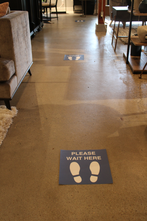 &quot;Wait here&quot; signs show customers where to stand to be at least six feet apart while wating near the checkout stand at Juxtaposition in downtown Camas.