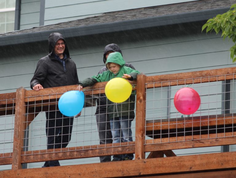 Timothy Hergenroether and his parents, Thomas and Jessica, stand on a balcony outside their Camas home on Sunday, May 3, as a parade of volunteers drive their vehicles -- decked out with balloons  and happy birthday signs -- around the street to help celebrate Timothy's eighth birthday.
