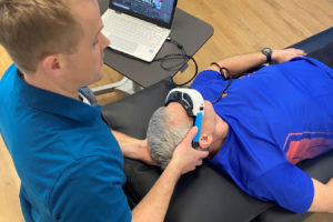 Physical therapist Mike Teater (left), co-owner of the Camas-based FYZICAL Therapy and Balance Center, demonstrates on a volunteer the postures and infrared goggles used to help treat a form of vertigo that can cause severe dizziness. (Photo courtesy of Mike Teater, FYZICAL Therapy and Balance Centers)