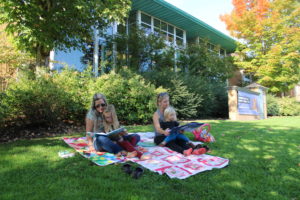 A family reads books outside the Camas Public Library on Oct. 9, 2020. Pictured are Cheryl Markwood, of Michigan (left), Janice Cole, of Camas (right), and Cole’s children, 5-year-old Zoe (on Markwood’s lap) and 2-year-old Henry (on Cole’s lap).  (Kelly Moyer/Post-Record)