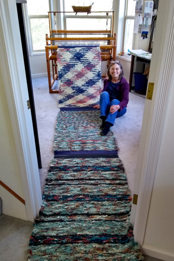 Washougal weaver Kathy Marty sits near a few of the rugs she has crafted using selvage cotton and wool from Pendleton Woolen Mills. (Contributed photo courtesy of Kathy Marty)