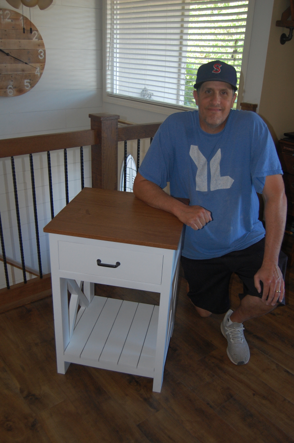 Washougal resident Greg Lewis sits next to a nightstand that he built.