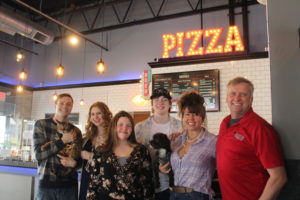Eric Duensing and John Strocko, co-owners of Camas Slices, gather with family inside the new Camas pizza shop on April 9, 2021. Pictured from left to right: John Strocko (holding Captain Jack the Bengal cat); John's wife, Melissa Strocko; Duensing's stepchildren, Charlie Young and Addison Young; Duensing's wife, Karista Young (holding Jack the dog); and Eric Duensing. (Kelly Moyer/Post-Record)