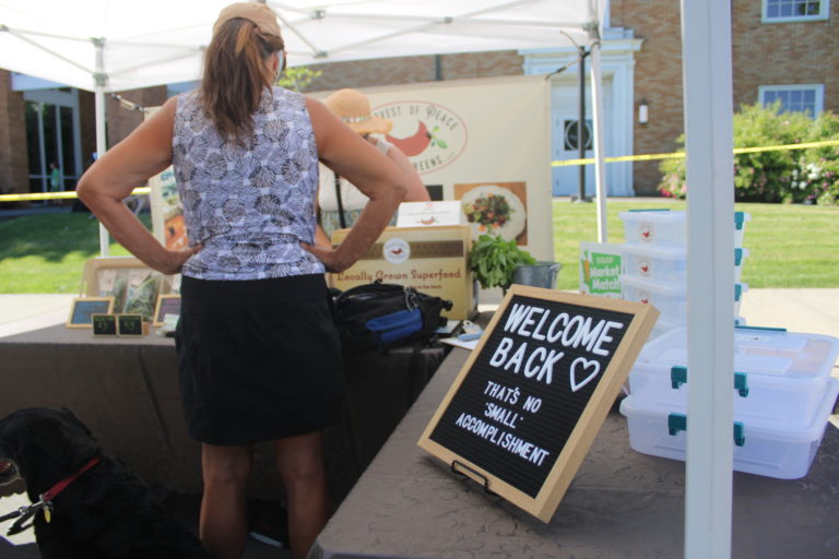 A sign welcomes visitors back to the Camas Farmers Market at the Harvest of Peace microgreens booth on Wednesday, June 2, 2021. (Kelly Moyer/Post-Record)