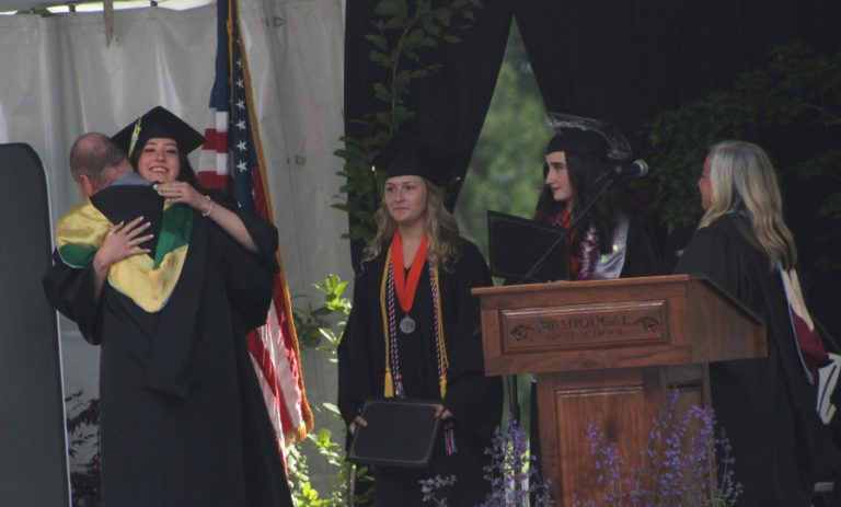 Doug Flanagan/Post-Record 
 Washougal High School graduate Amy Justis (left) hugs drama teacher Kelly Gregersen after receiving the Fran McCarty Award during the Washougal High School class of 2022 commencement ceremony at Fishback Stadium on Saturday, June 11.  Graduates Taylor Poulsen (second from left) and Alexis Perry (second from right) were named as the winners of the school&#039;s Citizenship and Black and Orange awards, respectively.