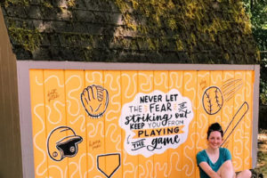 Camas resident Kadie Frazier sits next to a mural she painted on an East County Little League equipment shed at Lower Hathaway Park, in Washougal, during the summer of 2022. (Contributed photos courtesy of Kadie Frazier)