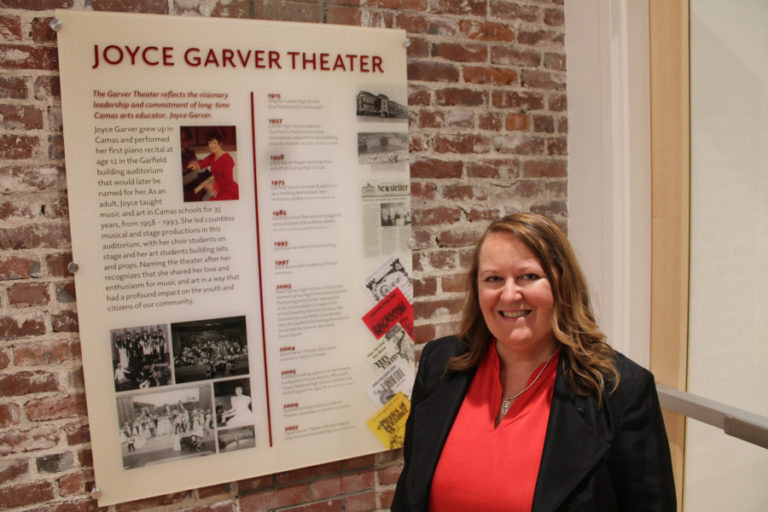 Julie Garver, the daughter of former Camas music teacher Joyce Garver, stands near a sign honoring her mother inside the Camas School District's newly renovated Joyce Garver Theater on Wednesday, Oct. 19, 2022.