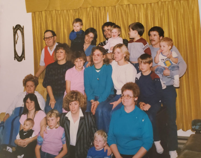 Ken and Ruthie Shold (far left, standing in red vest and seated in white shirt) gather with their children and grandchildren in 1983.