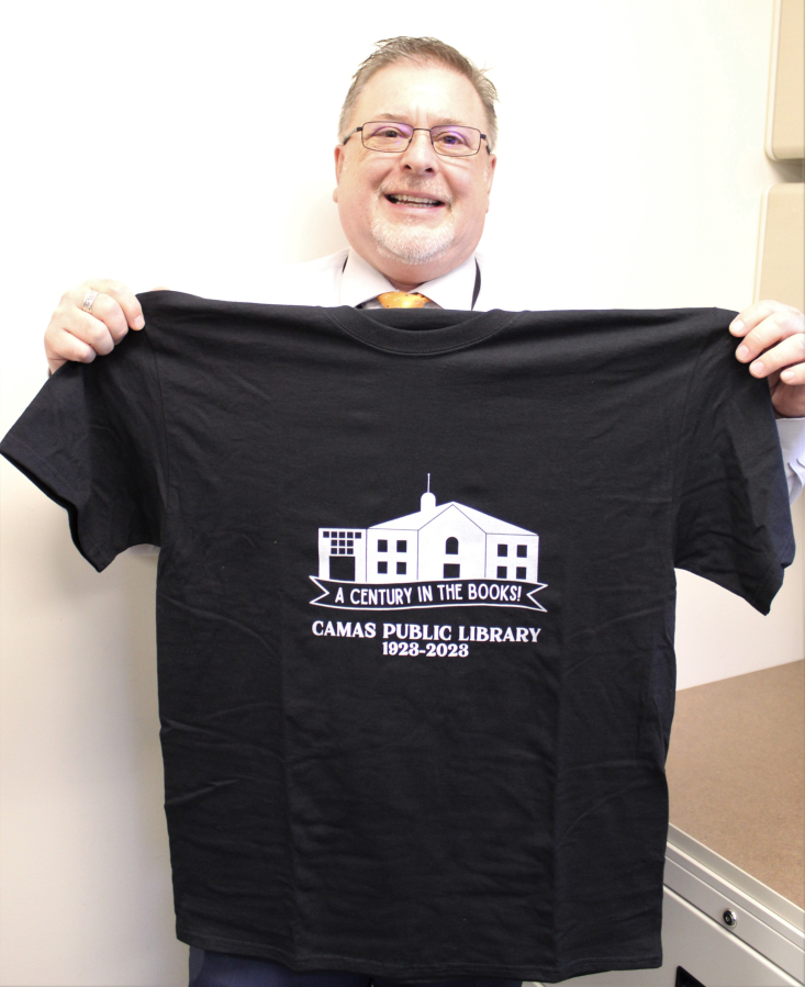 Christopher Knipes, an administrative assistant at the Camas Public Library, holds a T-shirt featuring the library&#039;s 100th anniversary &quot;A Century in the Books&quot; slogan on Friday, Oct. 28, 2022.
