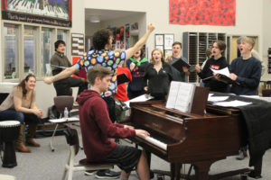 Camas High School (CHS) choir teacher Ethan Chessin (standing behind piano) conducts his first-period choir on Friday, March 17, 2023, while 2022 CHS graduate Brian Bishop (seated at piano) plays a piece he composed for the class, and singer-songwriter Brenna Larsen (far left), also a former CHS choir student, watches. (Photos by Kelly Moyer/Post-Record)