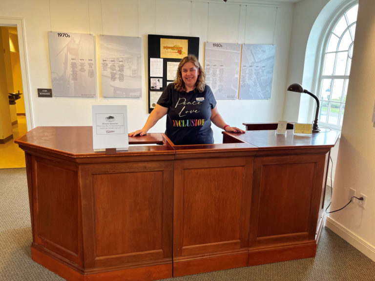 Camas library trustee Kerry Ticknor stands behind a vintage library desk from the 1940s inside the library's Second Story Gallery, during a history-themed First Friday event on April 7, 2023. (Kelly Moyer/Post-Record)
