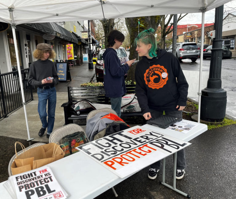 Discovery High School students Jax Goetzen (right), Angel Harp (center) and Zimri Baxter gather at a booth on the corner of Northeast Fourth Avenue and Northeast Cedar Street in downtown Camas during the Downtown Camas Association's First Friday event on April 7, 2023. The students are calling for the Camas School District to reconsider budget cuts that will impact their project-based learning high school.
