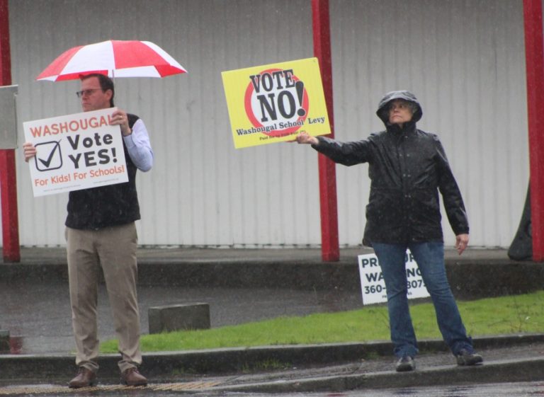 Washougal School District Assistant Superintendent Aaron Hansen (left) waves a &quot;vote yes&quot; sign while a community member waves a &quot;vote no&quot; sign on the corner of &quot;E&quot; Street and Washougal River Road on Monday, April 10, 2023.