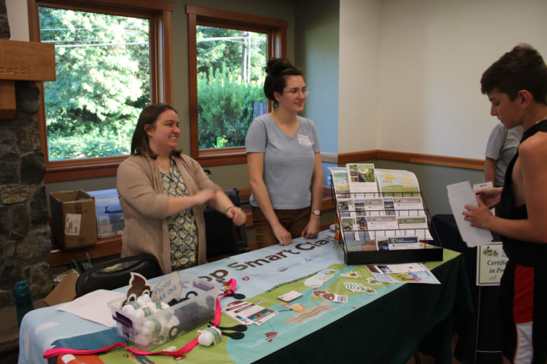 Grace DeMeo (left) and Carolyn Rice (right), with Clark Conservation District, talk to members of the public about the District's Poop Smart program, which offers financial assistance for people hoping to replace or repair failing septic systems and educates the public on the benefits of keeping animal feces out of the watershed, during a lake water-quality open house held Wednesday, July 12, 2023, at Lacamas Lake Lodge in Camas.