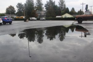 Nearby trees are reflected in a puddle covering multiple spaces in Washougal High School's student parking lot on Monday, Oct. 9, 2023. (Doug Flanagan/Post-Record)