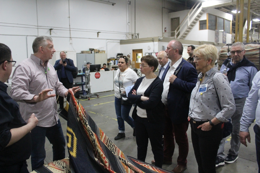 Tom Carroll, left, the executive vice president of operations of Pendleton Woolen Mills, shows a Pendleton blanket to a group of international visitors during a tour of the Washougal mill on April 19, 2023. (Doug Flanagan/The Columbian)