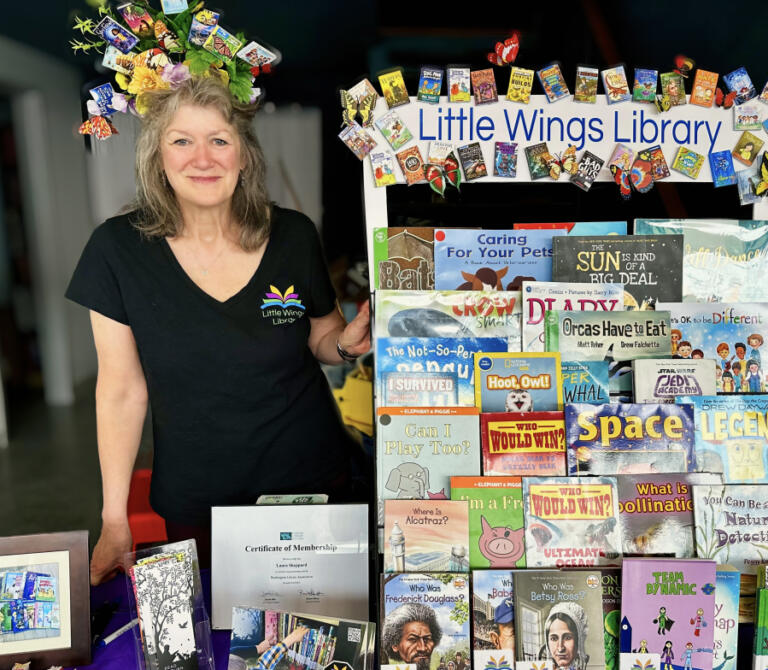 Laura Sheppard, a library paraeducator at Dorothy Fox Elementary School in Camas and the founder of Little Wings Library, a nonprofit dedicated to getting books to children through little lending libraries, sits next to a Little Wings Library display in Camas.