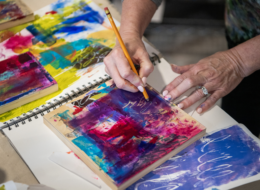 Artist Heidi Curley uses a pencil to write on a piece of paper at her studio in Camas Feb. 25. Curley uses art journaling, the process of journaling and then covering the words with paint, as a way to help release stuck emotions. (Taylor Balkom/The Columbian)