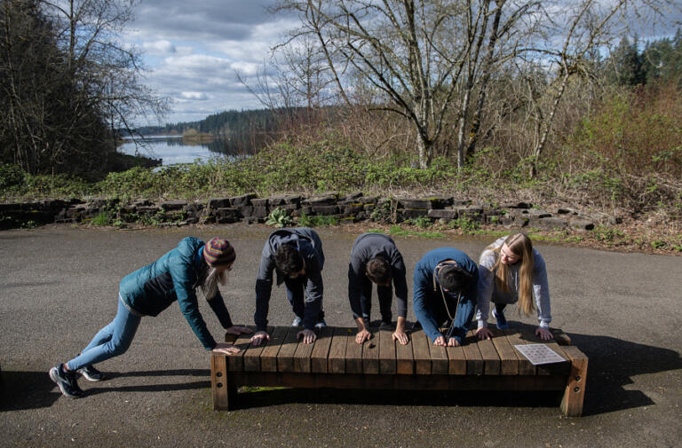 Volunteers Laura Hershberger, left, and Makena Campbell, right, lead athletes in the Mountain Tops class in pushups as they make their way along the Heritage Trail in Camas on April 3. Mountain Tops, a fitness program for young adults with physical, mental and emotional developmental disabilities, is held twice a week at Lacamas Lake Lodge in Camas.